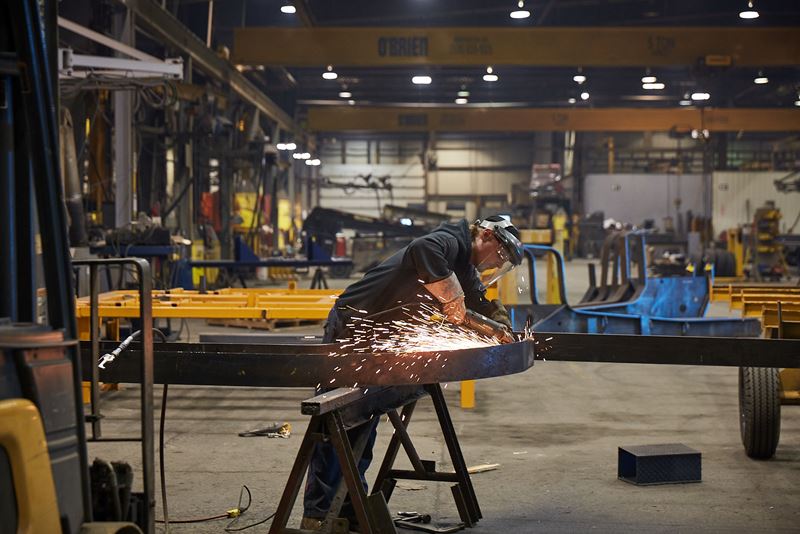 Un homme debout dans un grand atelier utilise une meuleuse métallique